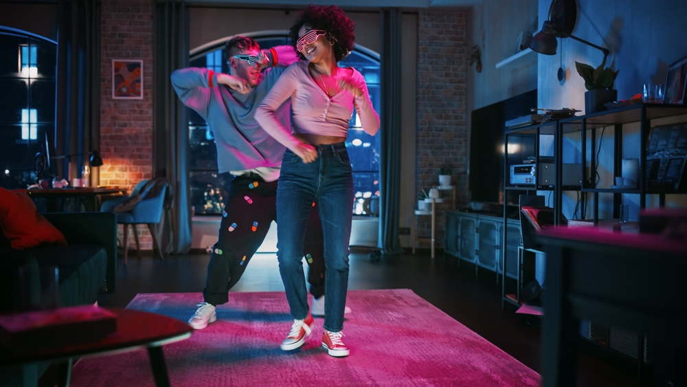 Beautiful Stylish Multiethnic Couple in Casual Outfits and Futuristic Neon Glowing Glasses, Dance and Have a Party at Home in Loft Apartment. Recording Funny Viral and Active Videos for Social Media.