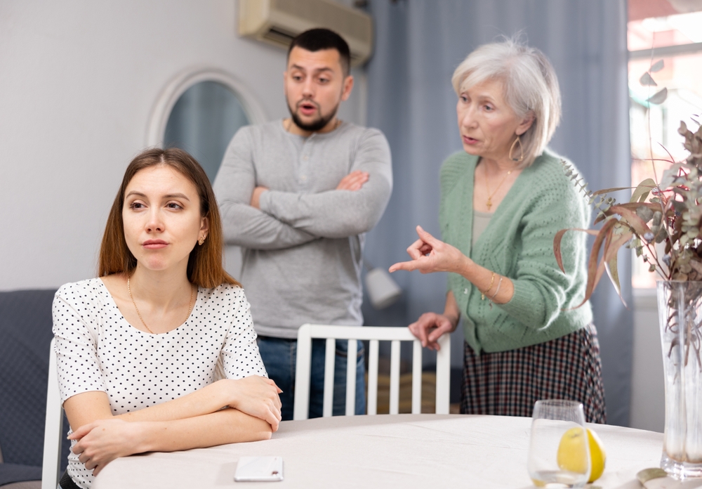 Woman ignoring her husband and mother-in-law standing behind and arguing with her at home.
