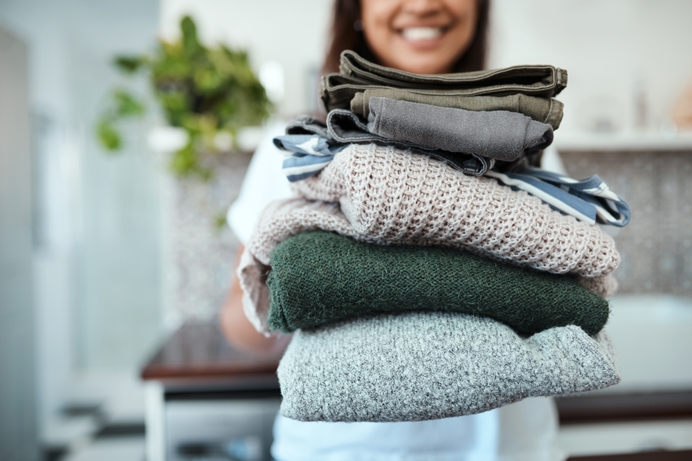 Stacked and ready to be packed. Closeup shot of a young woman holding a pile of folded laundry at home.