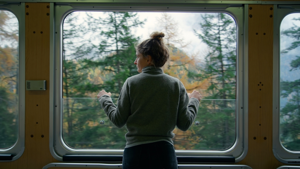 Cinematic and symmetrical beautiful shot of female traveler, travel blogger and inspired adventurer hang out of train window, look at amazing landscape of autumn mountains
