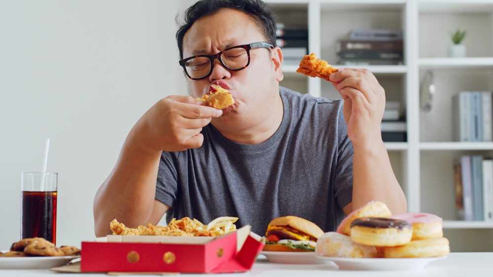 Asian fat man enjoy to eat unhealthy junk food, hamburger, pizza, fried chicken
