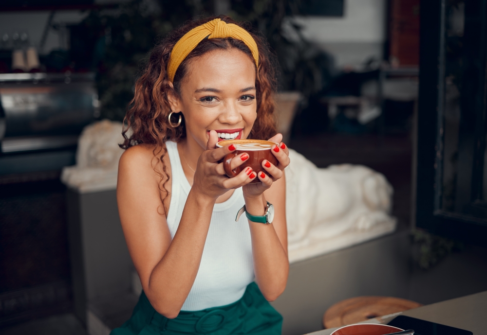 Smile, happy and coffee shop young woman enjoying a cup of tea in a restaurant or cafe on her lunch break. Portrait of happy customer drinking her morning caffeine or cappuccino with happiness

