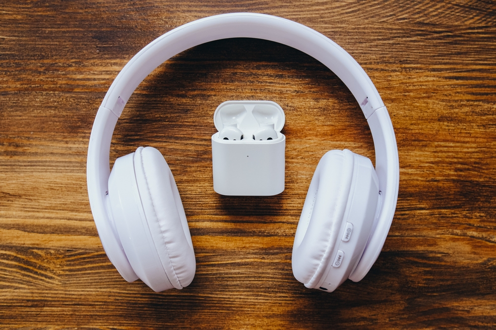 Full size big headphones vs small earbuds. Big and small white earphones on a wooden table.
