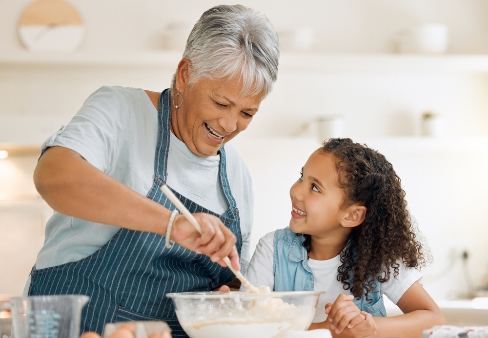 Grandmother, happy or child baking in kitchen as a happy family with young girl learning cookies recipe. Mixing cake, development or grandma smiling or teaching kid to bake with eggs, butter or flour