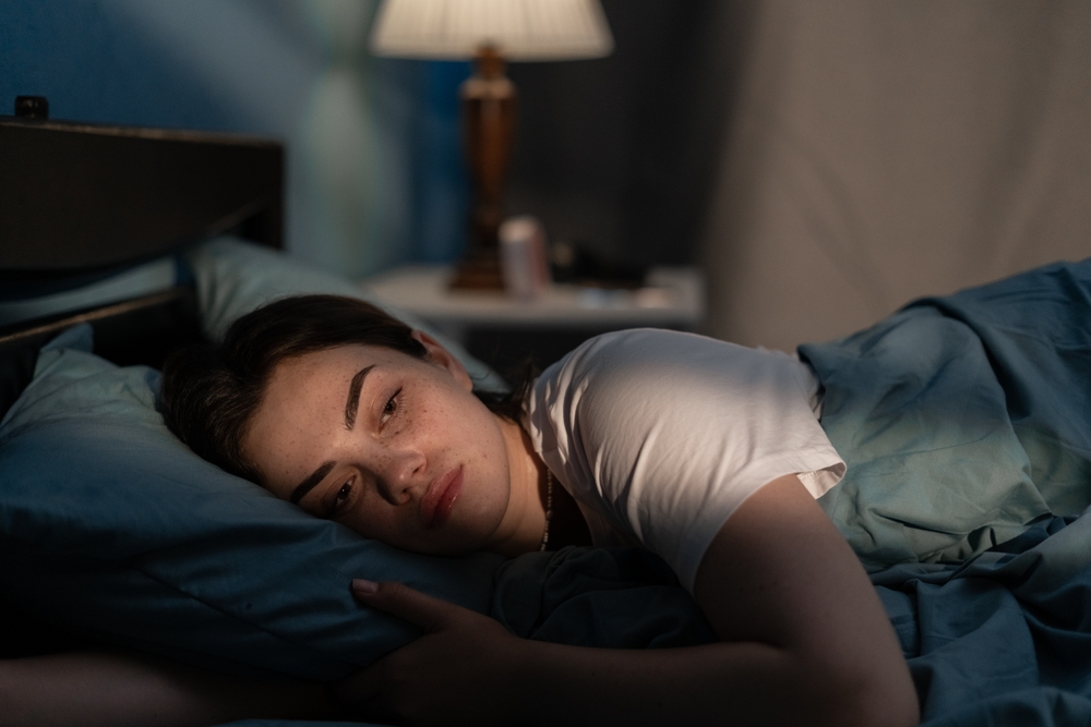 Young sad woman lying in bed late at night trying to sleep suffering insomnia. Girl in bed scared on nightmares looking worried and stressed. Sleeping disorder and insomnia concept
