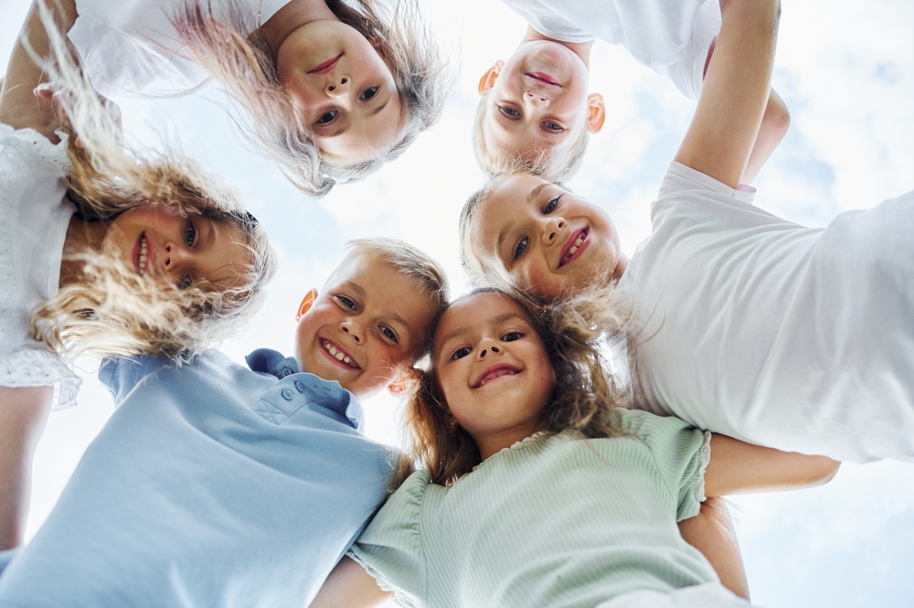 View from below of happy kids that are standing together and looking down.