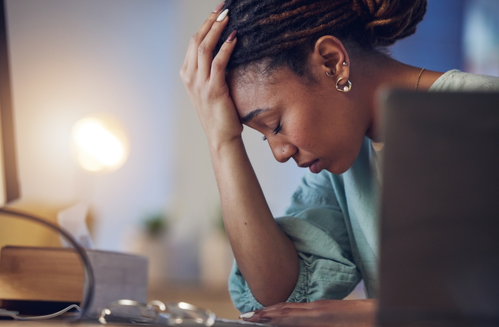 Business woman, depression and stress in an office at night working late on deadline. Tired African entrepreneur person with hands on head for pain, burnout or regret for mistake or fail at work
