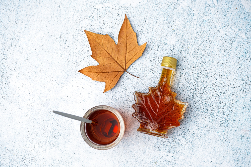 Bottle and glass of tasty maple syrup on grey background
