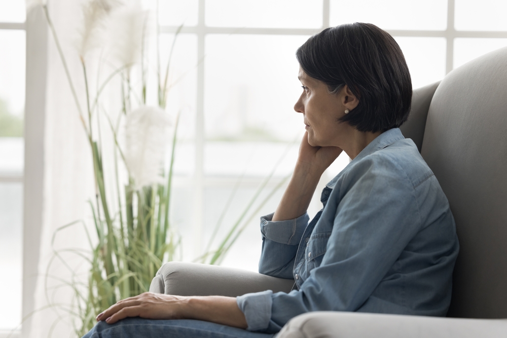 Pensive mature woman sits on armchair staring into distance, deep in thoughts, pondering, thinks on life problems, spend time alone at home, suffering from solitude and boredom on retirement. Concerns
