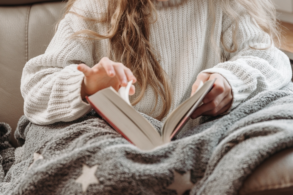 Young woman reading book,A cold fall or winter weekend while reading a book. A lazy day, a girl covered with a blanket is reading a book