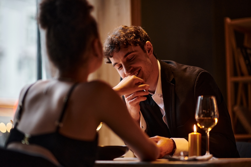 happy gentleman in elegant attire kissing hand of girlfriend during date on Valentines day