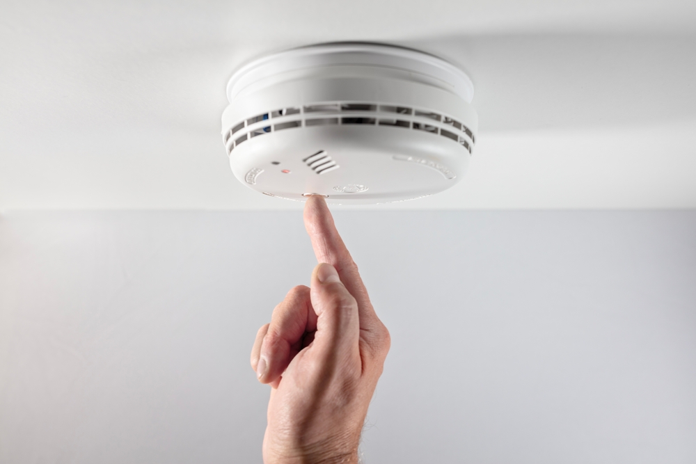 Home smoke and fire alarm detector maintenance man pushing button checking, testing or replacing battery
