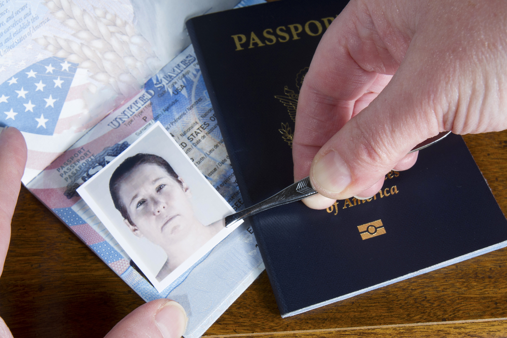 Hand with tweezers holding id photo over passport as if forging the travel documents
