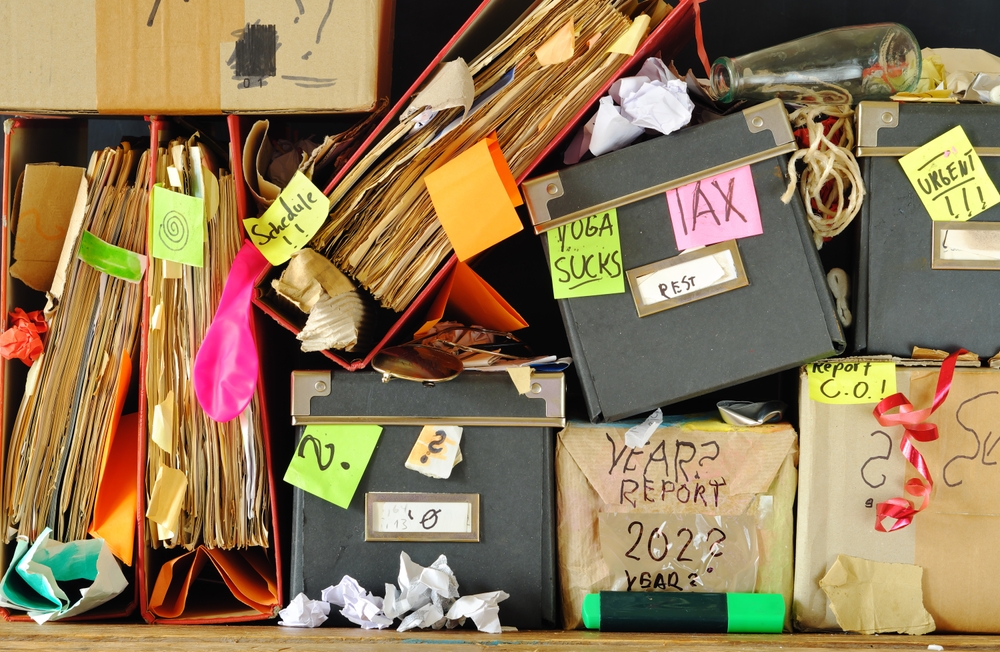 messy file folders and storage boxes in a cluttered office bookshelf,red tape,bureaucracy,overworked,business concept,free copy space.
