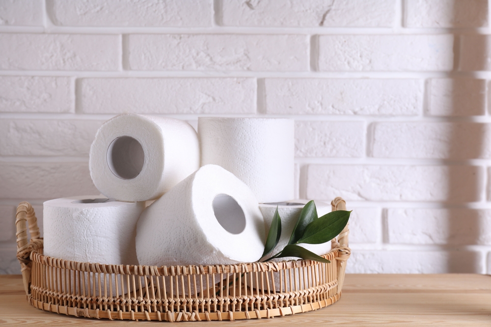 Toilet paper rolls and green leaves on wooden table near white brick wall
