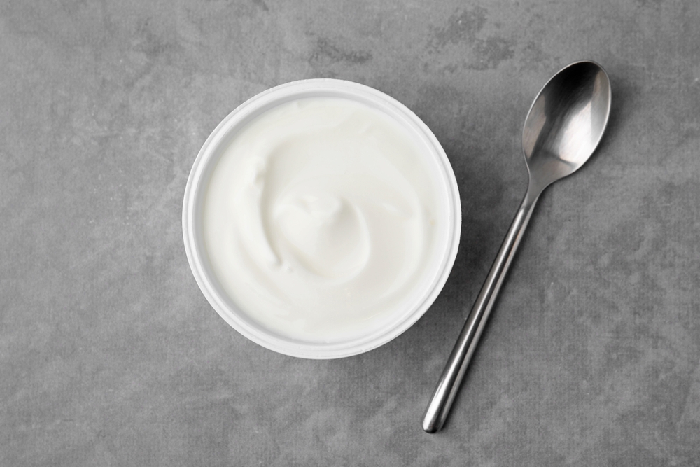 Delicious natural yogurt in plastic cup and spoon on grey table, top view

