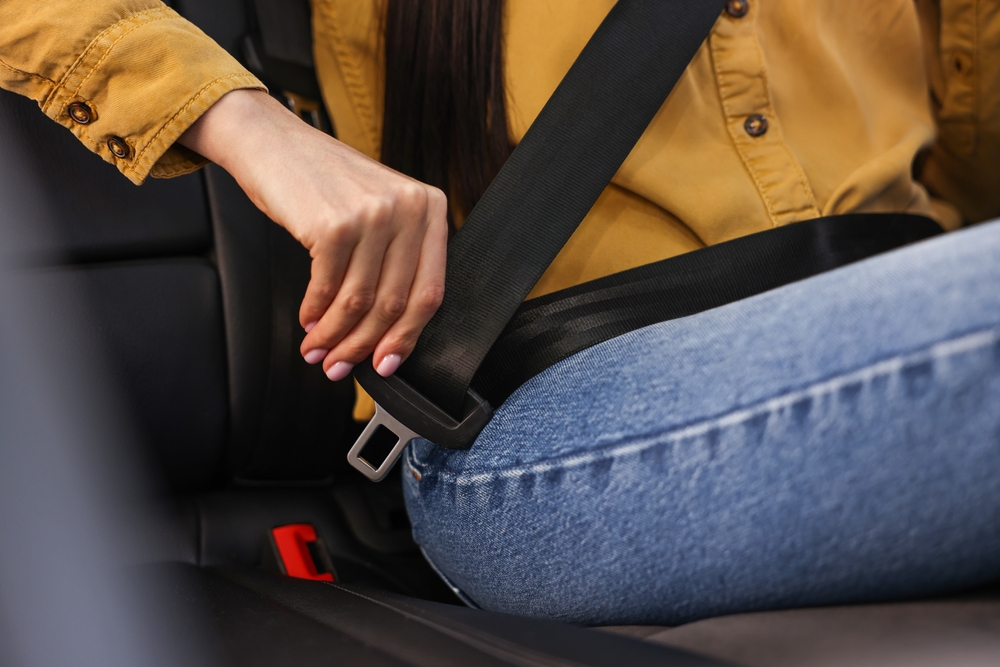 Woman fastening safety seat belt inside modern car, closeup
