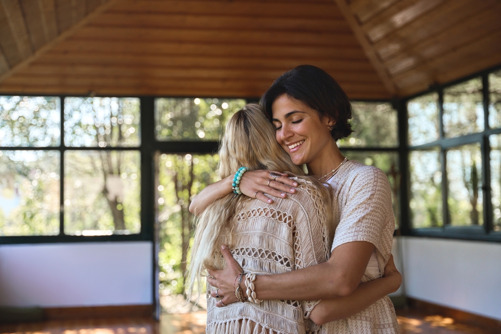 Happy female holistic coach hugging young woman during spiritual practice feeling gratitude and love, giving psychological help support during body health retreat healing recovery training session.