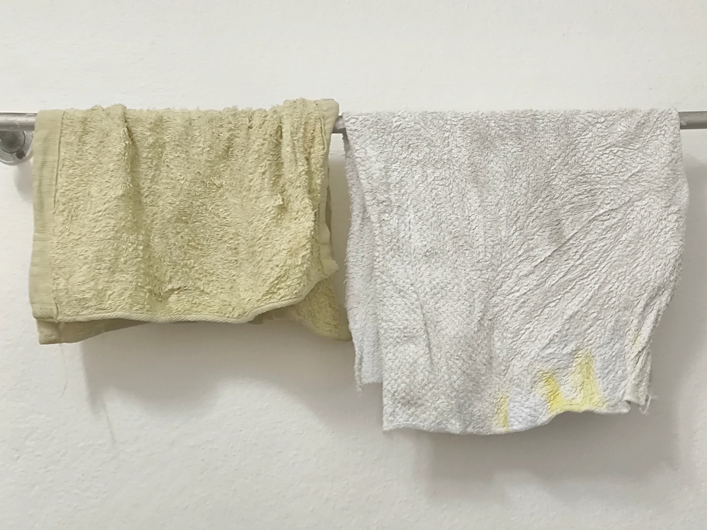 Dirty rags hanging on stainless towel hanger on white concrete wall with copy space
