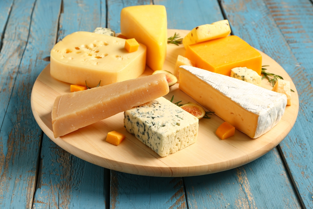Board with tasty cheese on blue wooden background