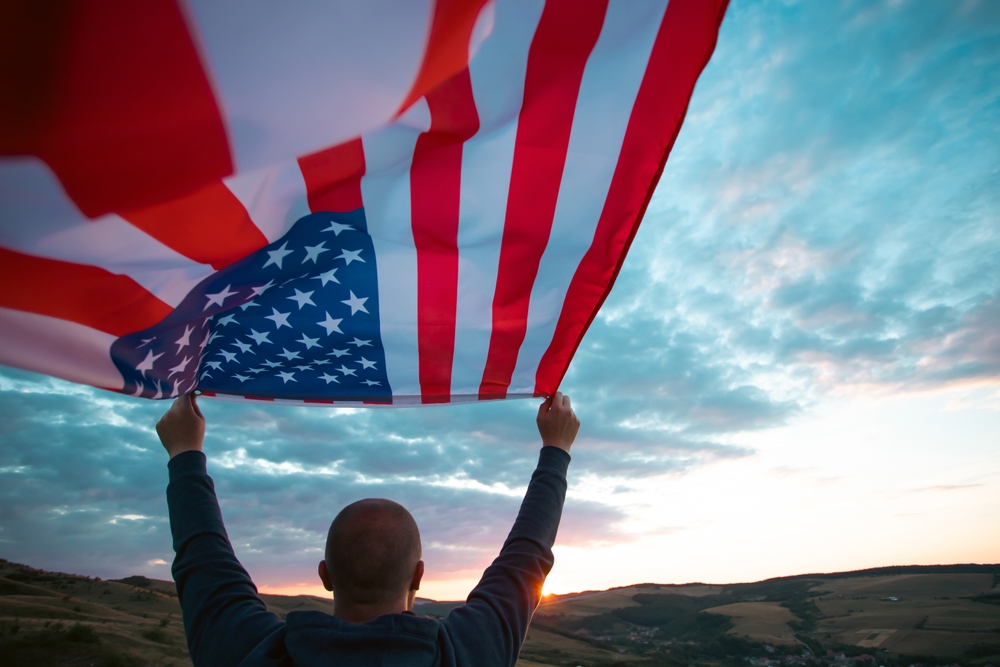 Man holding american USA flag in the sunset. Independence Day or traveling in America concept.