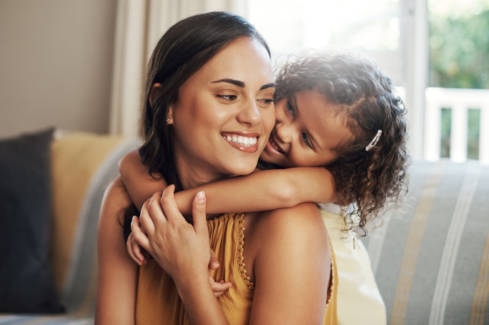 Mom, girl and hug with love on sofa for bonding with affection, safety and childhood security for support. Mother, child and relax with care in living room of home, together and nurture connection.