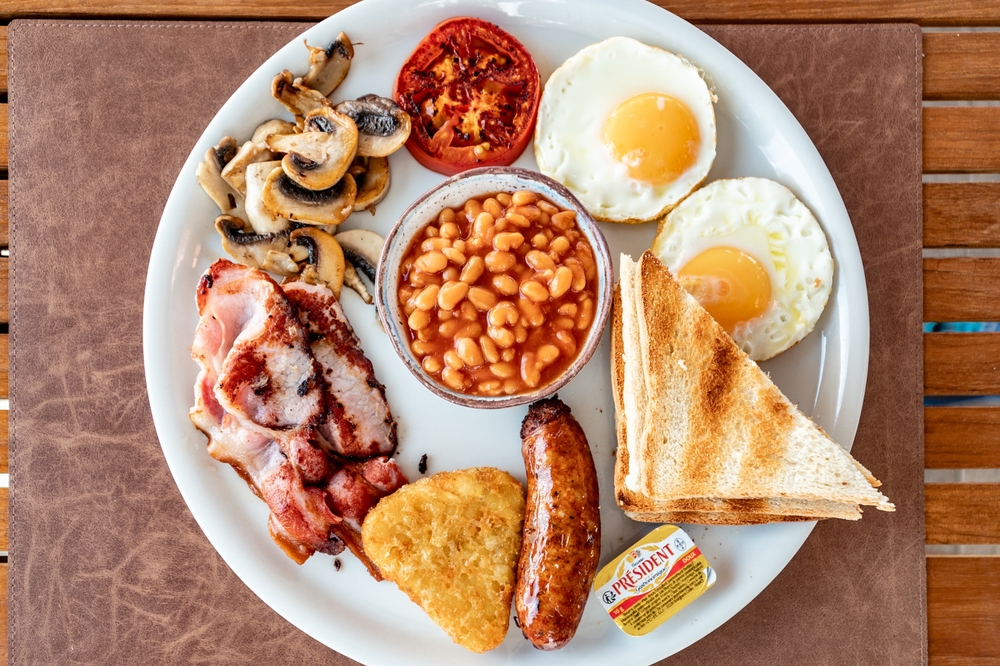 a close up birds eye view image of a full English fried breakfast on a wooden table.
