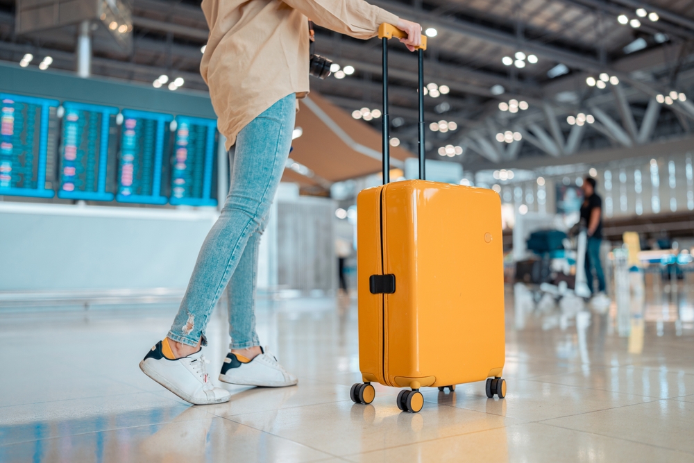 Young female traveler passenger walking with a yellow suitcase at the modern Airport Terminal, Back view of woman on her way to flight boarding gate, Ready for travel or vacation journey