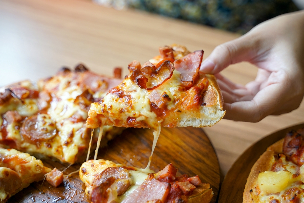 Hand holding pizza slice from tray. it is an Italian fast food consisting of a flat round dough topped with tomato sauce. Then cooked by baking in the oven.