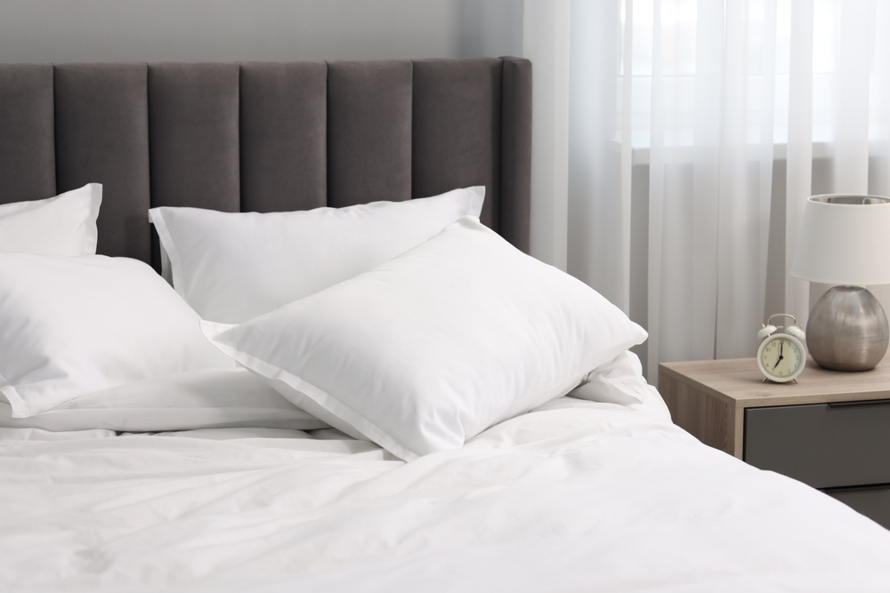 Many soft pillows on bed and bedside table at home
