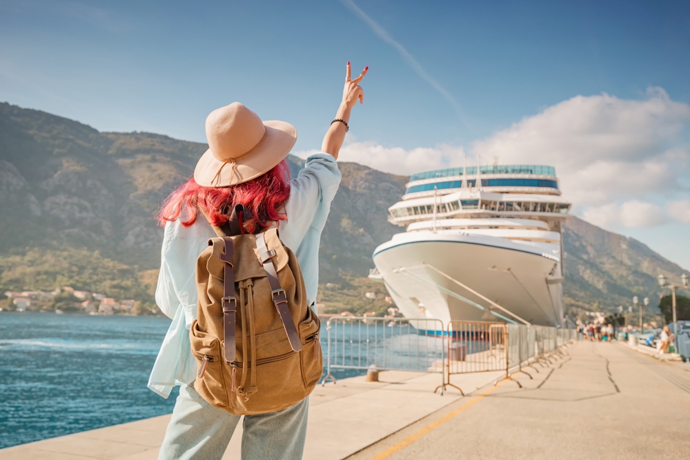 Tourist wearing backpack and hat gesturing near cruise ship at Kotor bay, Montenegro