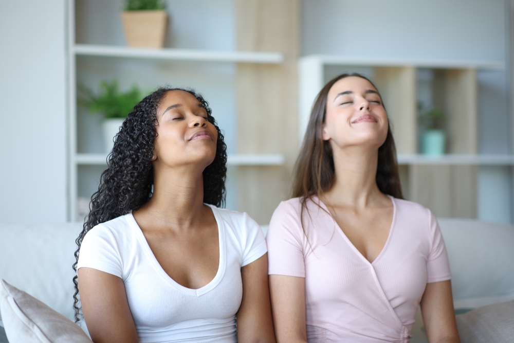 Two relaxed interracial roommates breathing fresh air at home

