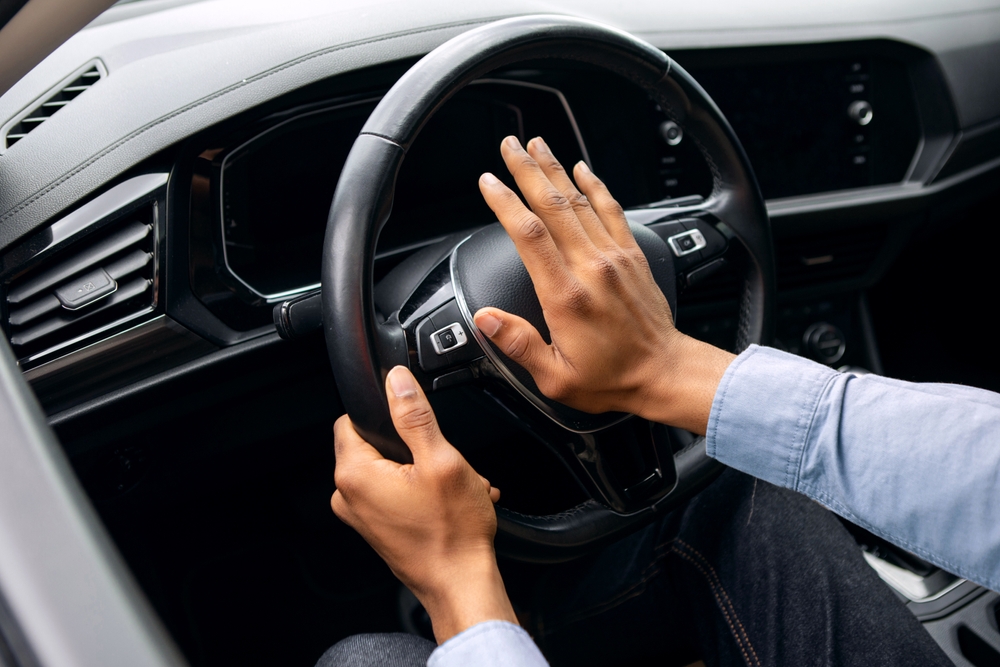 Young black man honking while driving, sitting in car, holding steering wheel, beeping the horn in auto

