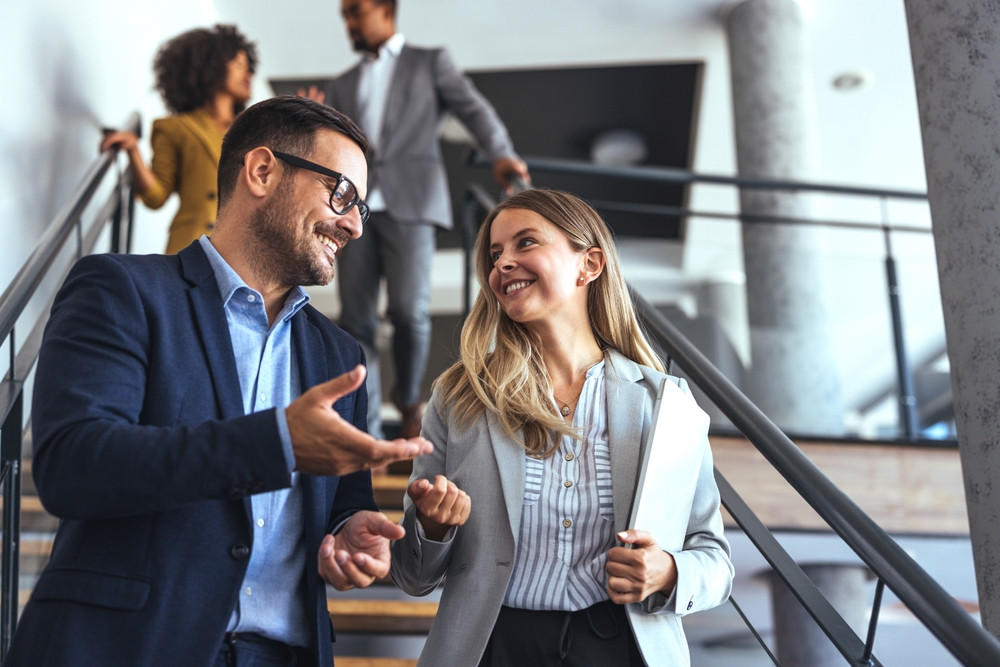 Professionals in a modern office environment discussing work-related matters on a staircase. A scene of positive collaboration, business attire, and a productive team atmosphere.
