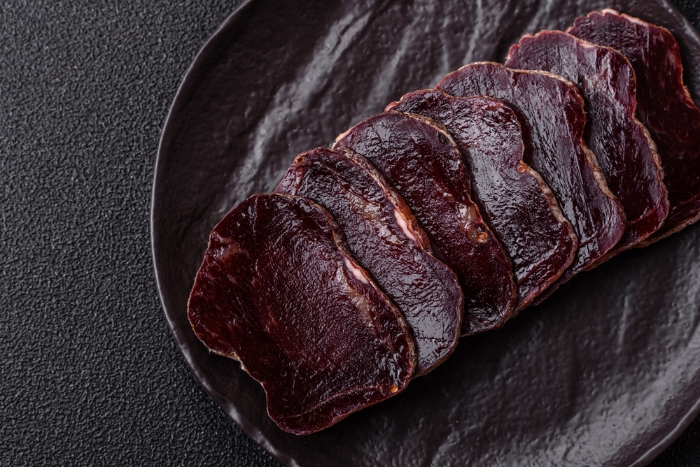 Smoked horse meat with salt, spices and herbs on a dark concrete background
