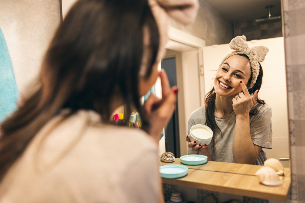 Woman doing her skincare routine in bathroom while putting cream on her face.