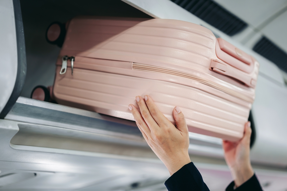 Close up view hands placing travel bag in overhead airplane storage preparing for international flight trip journey