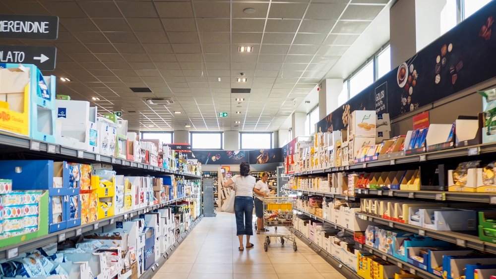 Cremona, Italy July 12nd 2025 Two women pushing shopping carts and buying groceries inside a brightly lit ALDI supermarket with shelves full of various products