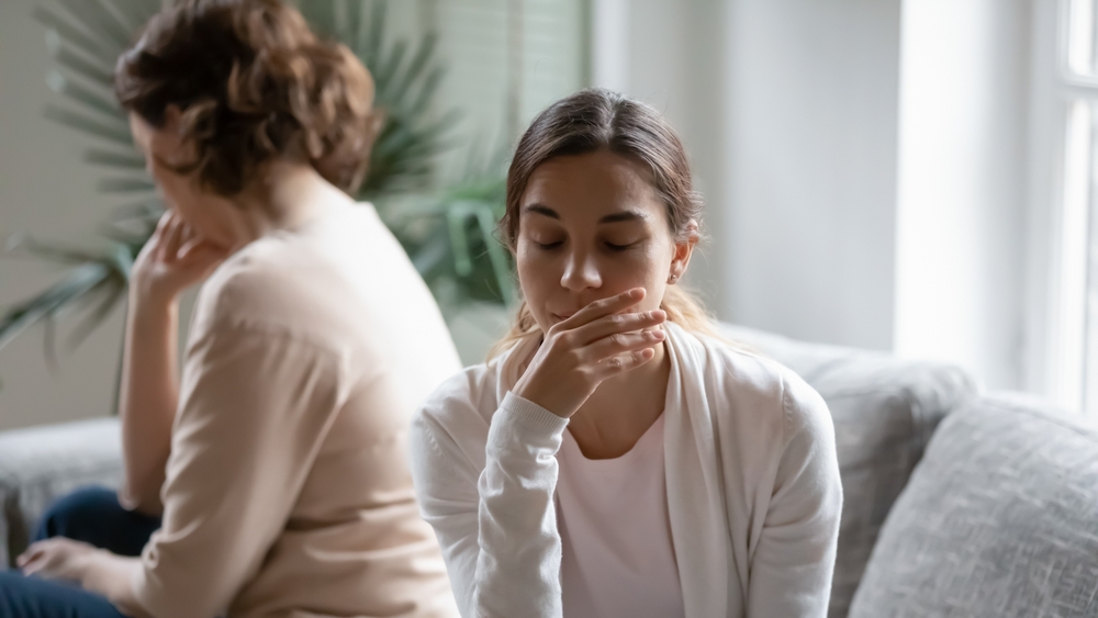 Frustrated young woman sitting back to back with stressed middle aged 60s mother, feeling disappointed after conflict at home. Unhappy different generations family ignoring each other after quarrel.