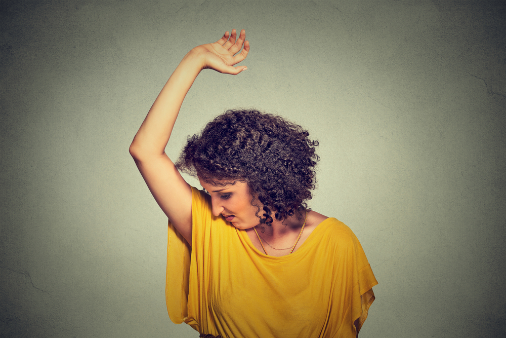 Closeup portrait young woman, smelling, sniffing her wet armpit, something stinks, very bad foul odor situation isolated grey wall background. Negative human emotion facial expression feeling reaction
