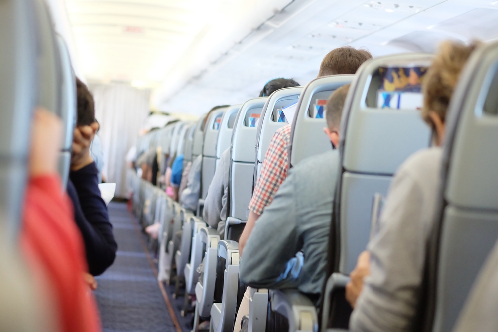 Passengers are sitting and sleeping on an airplane. They get stuck in their seat in a long and boring flight.