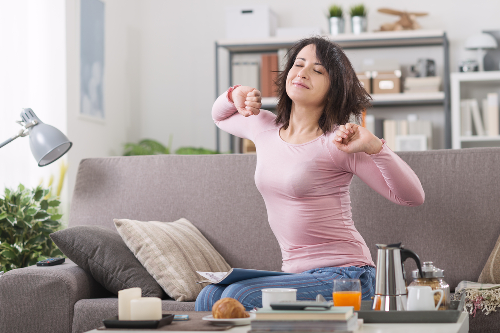 Young woman at home waking up after a bad night's sleep on the couch, she's stretching
