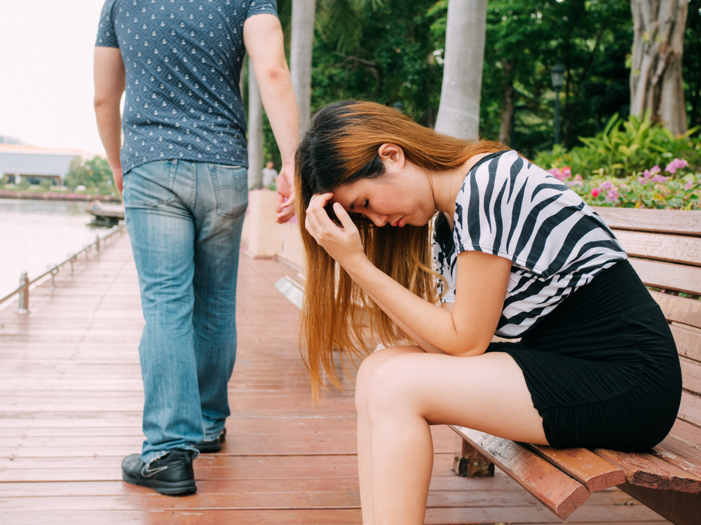 Breakup of a couple with sad girlfriend and boyfriend walking away with city in the background
