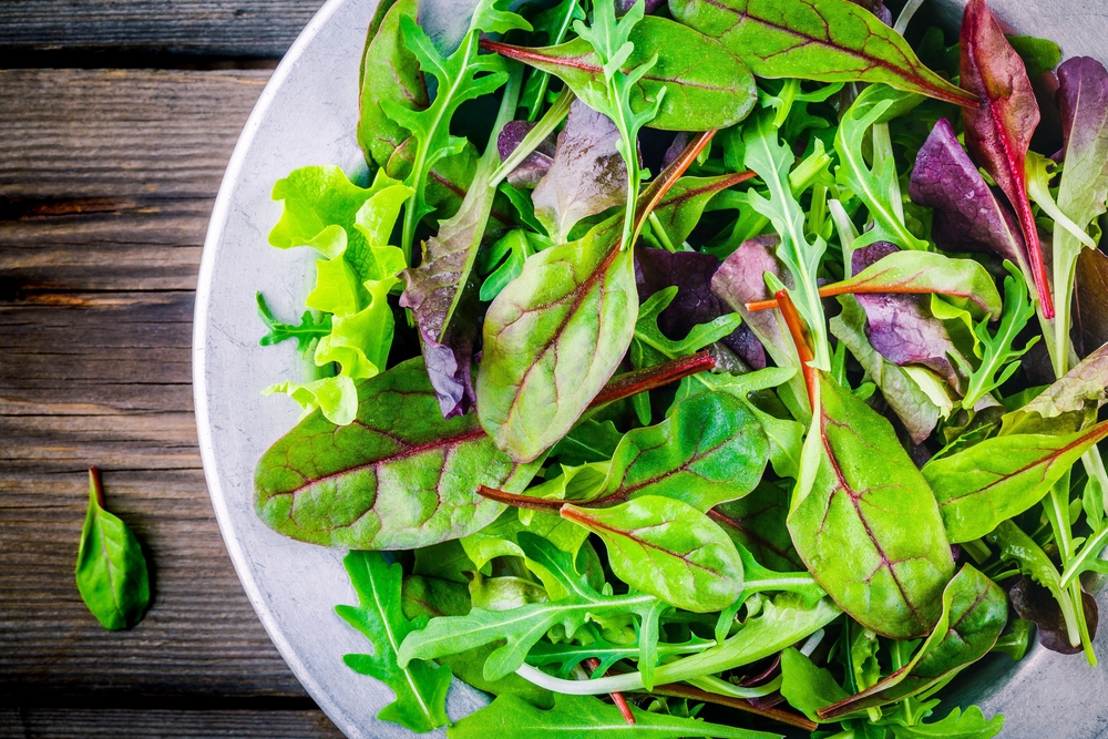 Fresh salad with mixed greens in bowl on wooden background closeup
