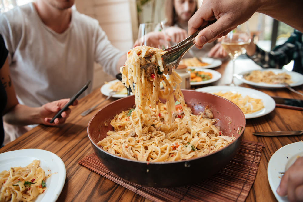 Closeup of group of people eating pasta on the kitchen at home