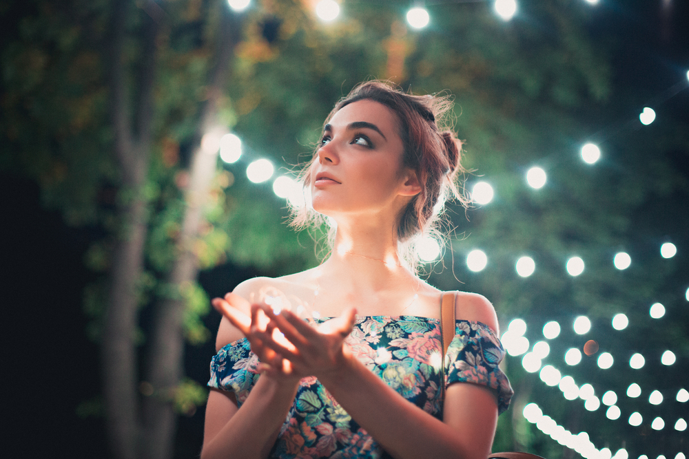 Beautiful young woman smiling and talking garlands of lights at city
