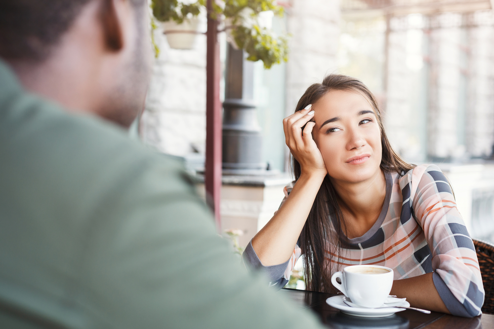 Young bored girl sitting and drinking coffee on date with her boyfriend at cafe. Speed dating, unsuccessful meeting