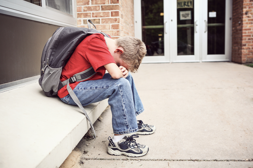 Depressed student sitting outside of school hiding his face