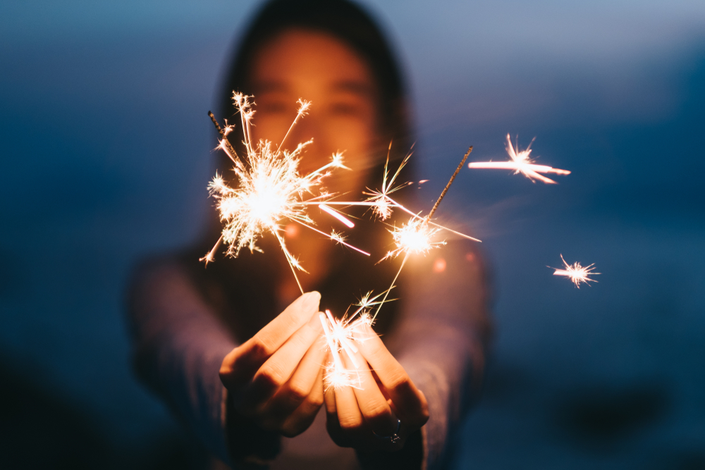Young happy woman stands on beach with sparkler in sunset light.