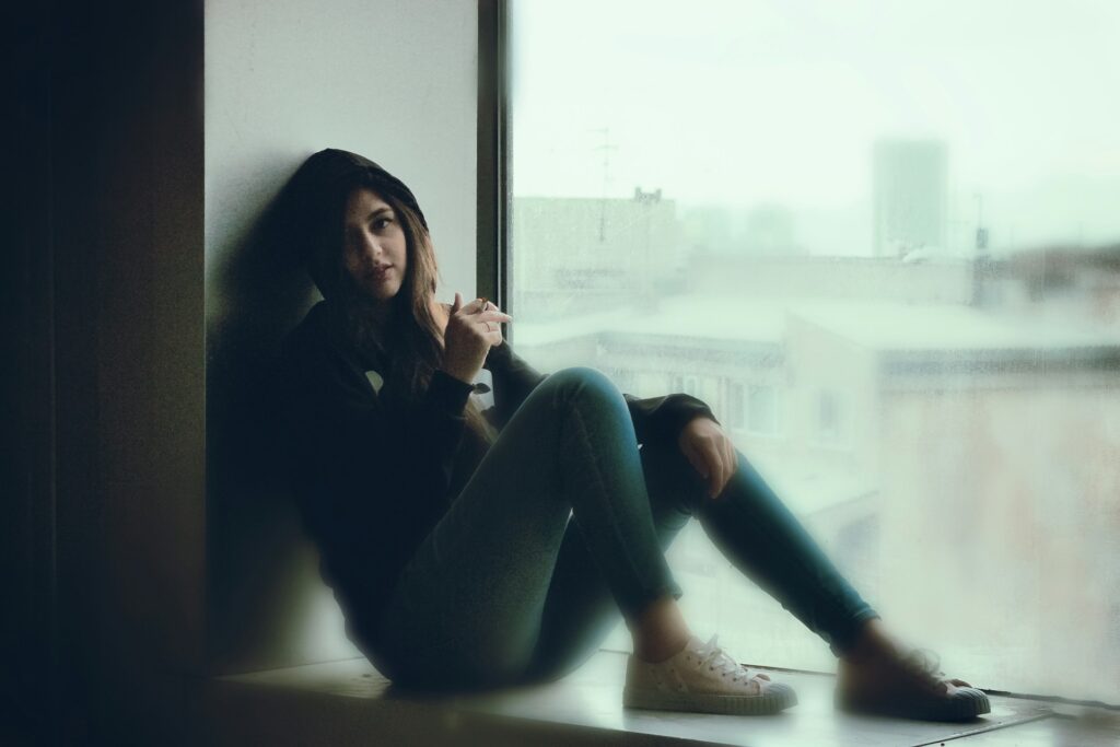 A woman sitting on a window sill looking out the window
